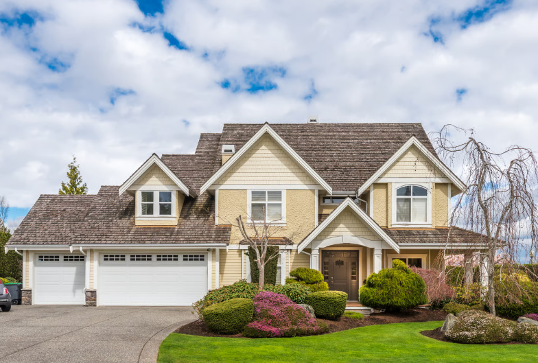 Two-story yellow suburban family home in Virginia with a grey shingle roof, a three-car garage, manicured green lawn, and landscaped garden under a cloudy blue sky.